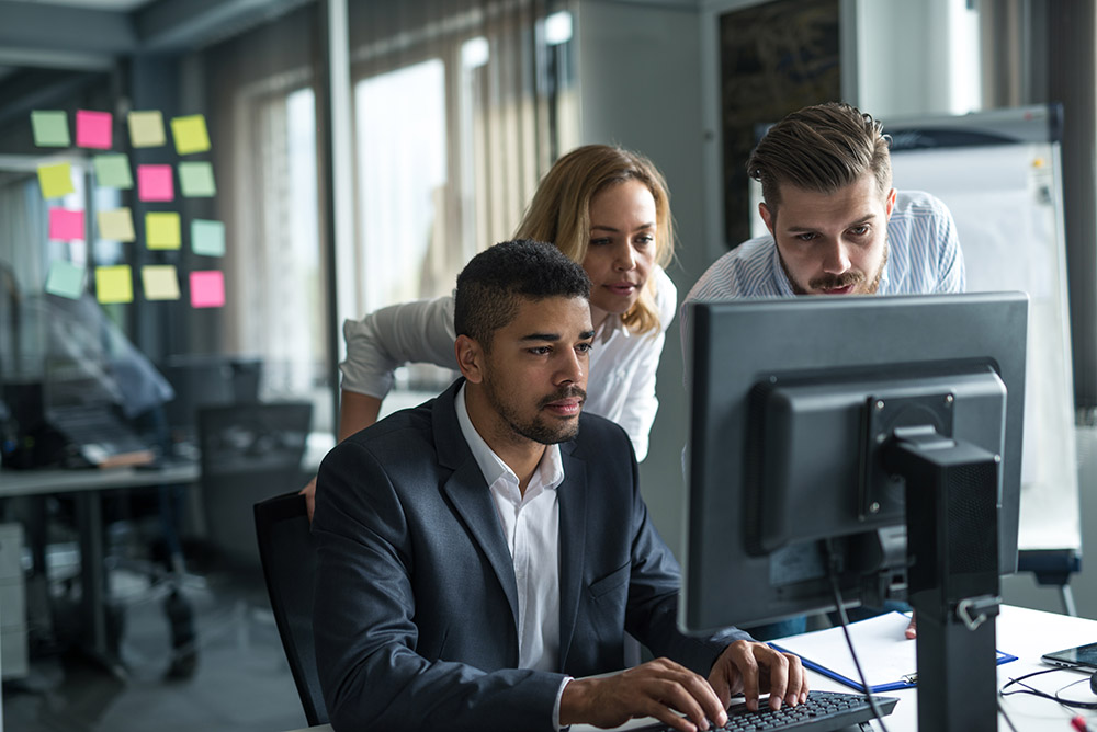 three business people in a conference room looking at a computer screen together.